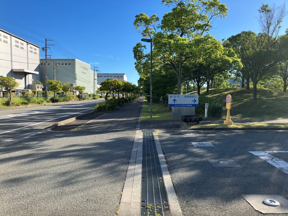 工場敷地入口の案内看板。左方向が物流門、右方向が来場者受付であることを示しています。