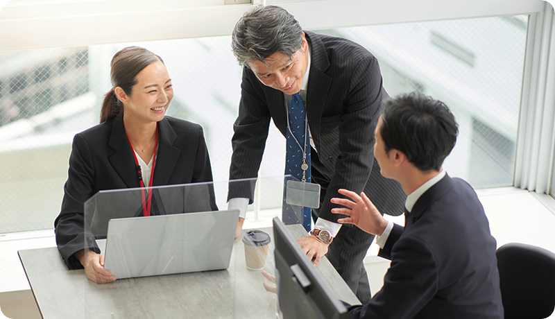 風通しの良い職場で、役職に関係なく上司と部下が笑顔で意見交換している様子