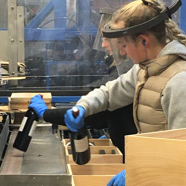 写真3：木箱へのワイン詰めも、フェイスシールド＋作業者を隔てるアクリル板を併用して実施。